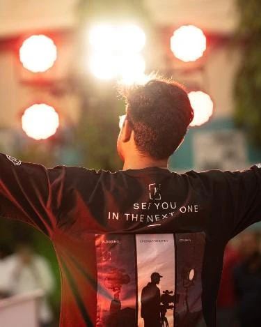 On stage under the lights, arms spread, in a See you in the next one T-shirt